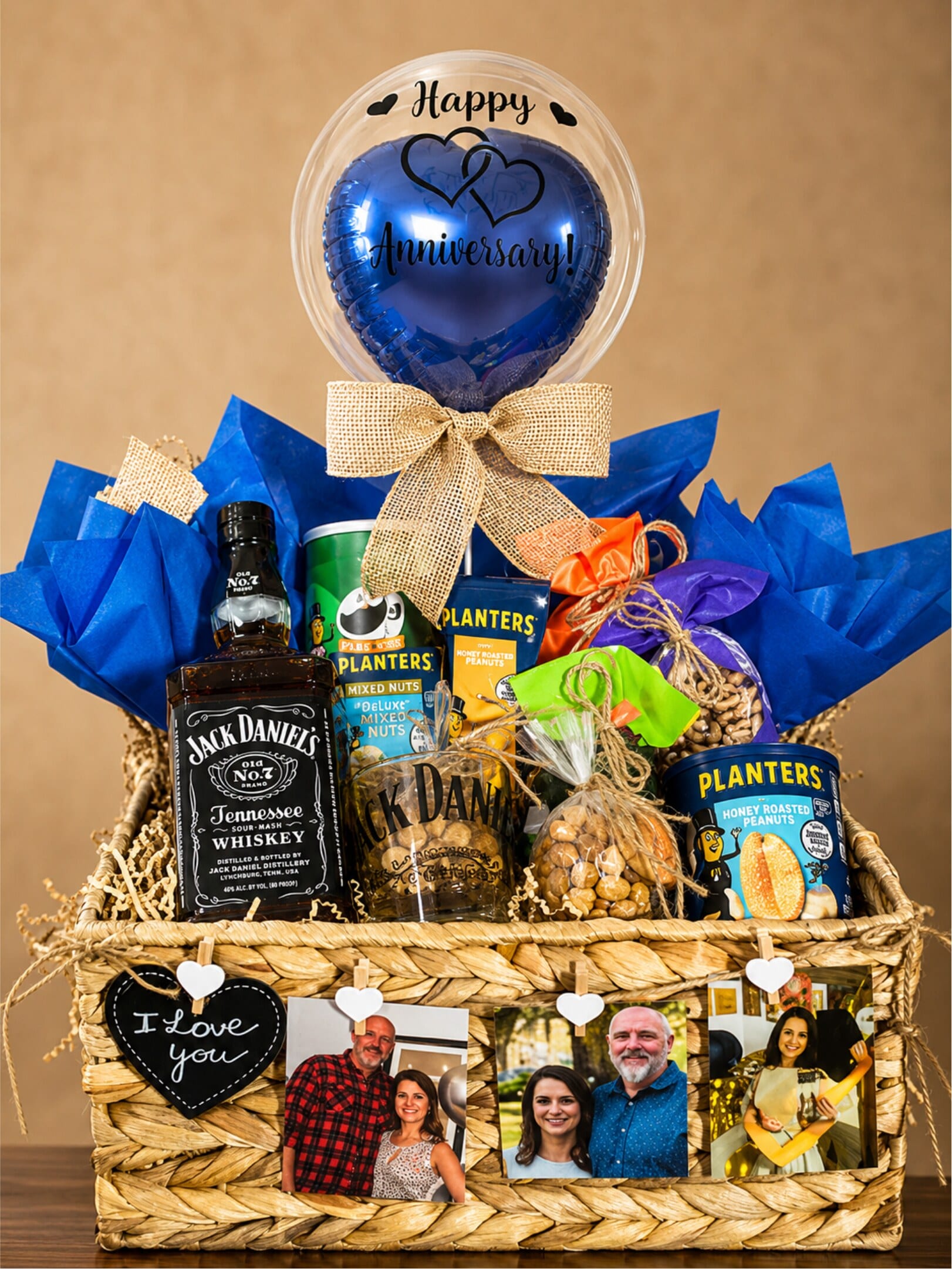 A blue personalised balloon above a rustic basket with whiskey, snacks, and framed family photographs.